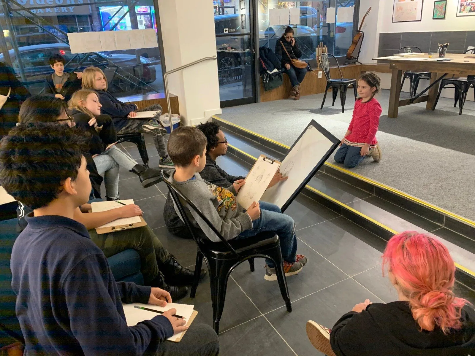 Students sit with sketchbooks drawing a model posed on the stepped stage during a figure drawing class.