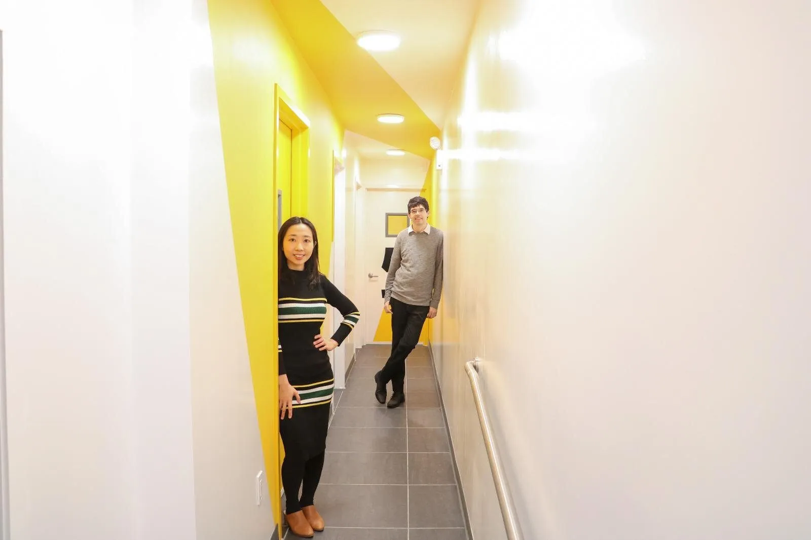 A long white hallway with a vertical yellow stripe on the left wall leading toward the studios.